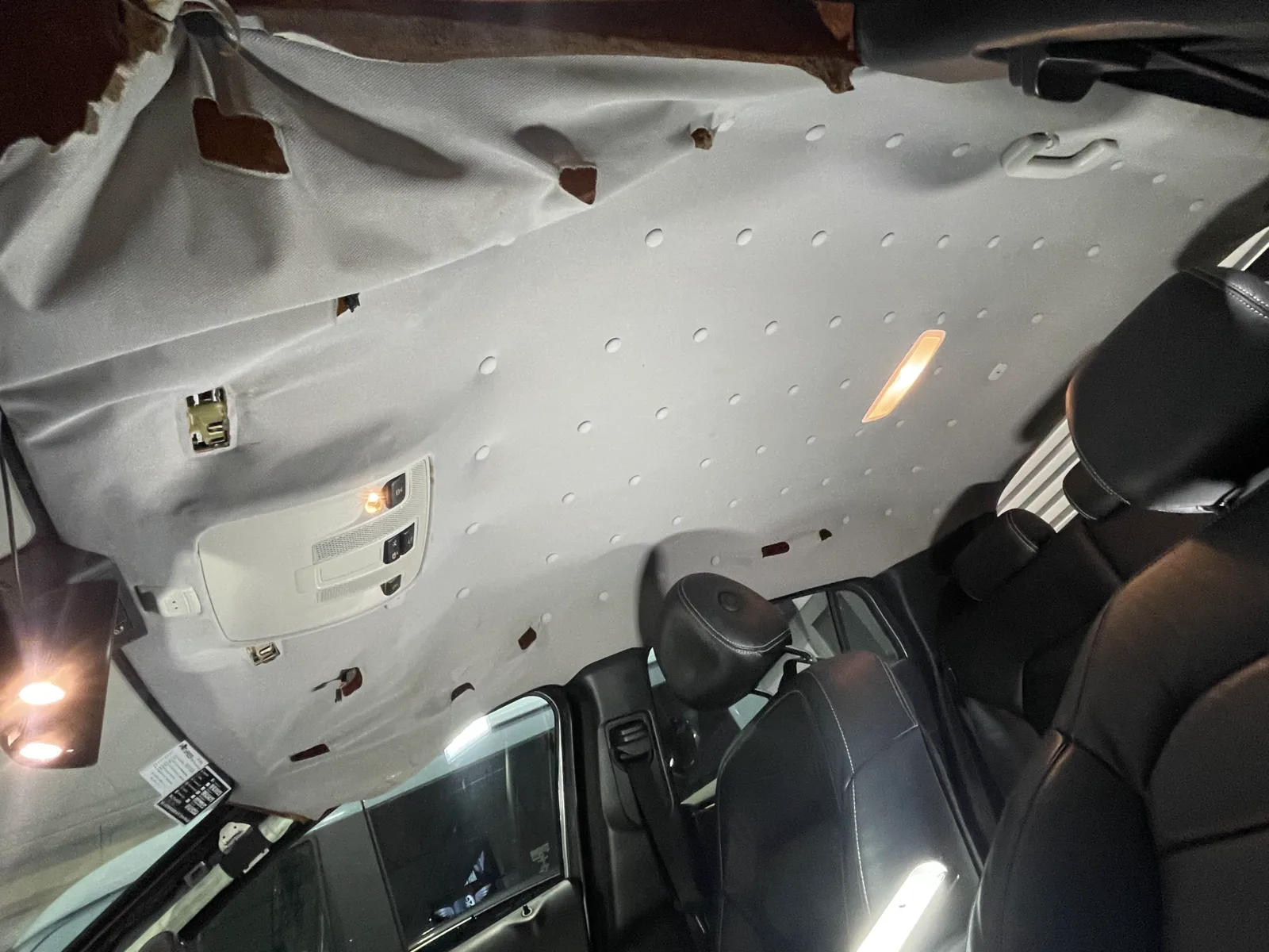 Actual car interior with sagging roof lining fabric held up by many plastic repair pins